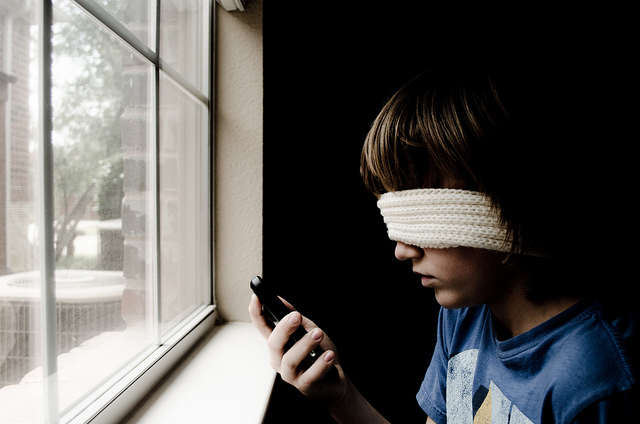 A blindfolded child tries and fails to look at a smart phone