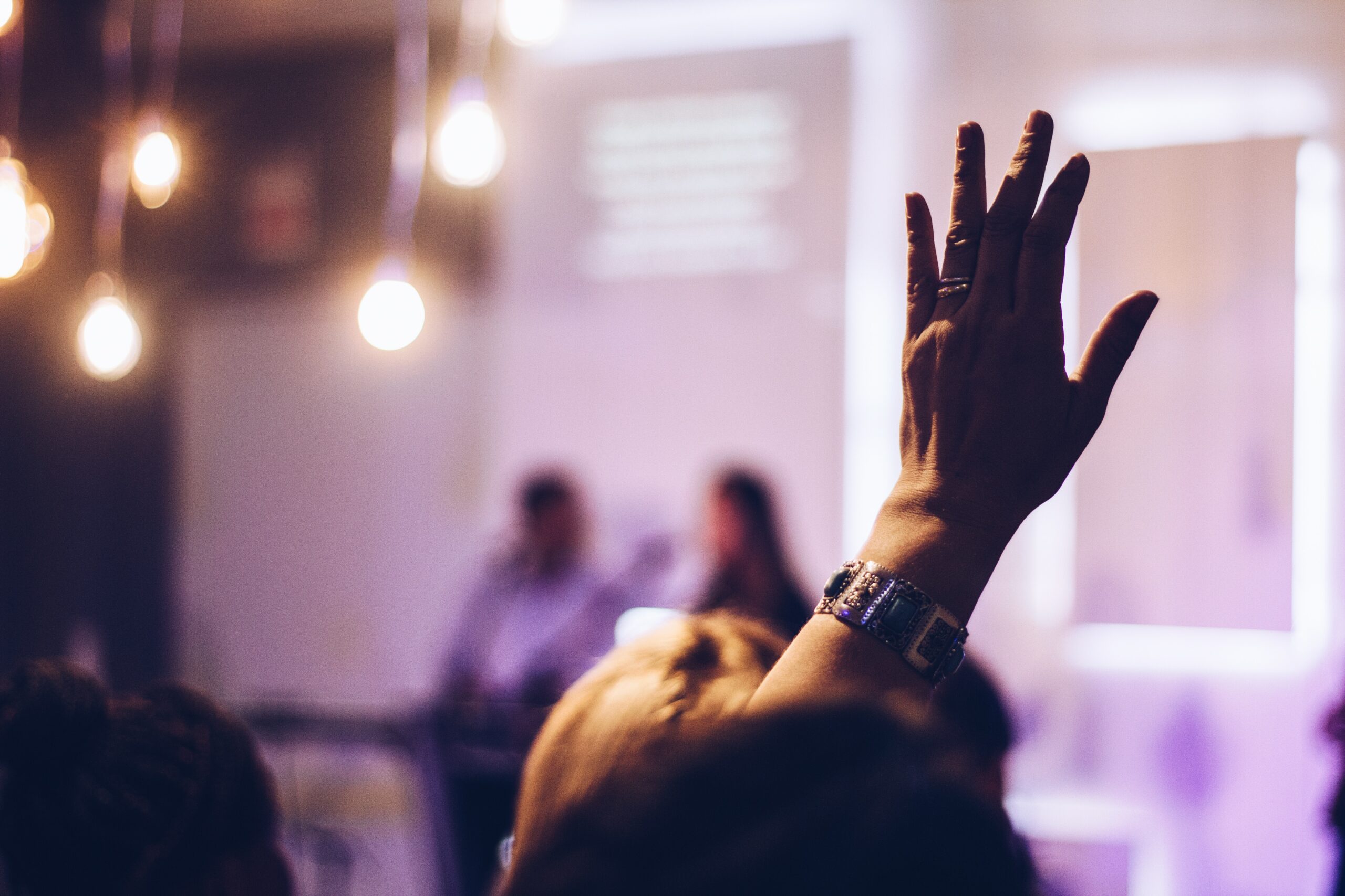 a person with light-colored skin and wearing a watch raises their hand in a classroom.  