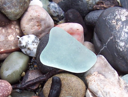 Turquoise sea glass resting against beach stones
