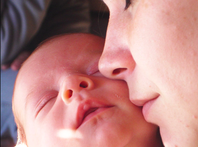 An image of a woman cradling a baby in her arms and resting her cheek against the baby's cheek.