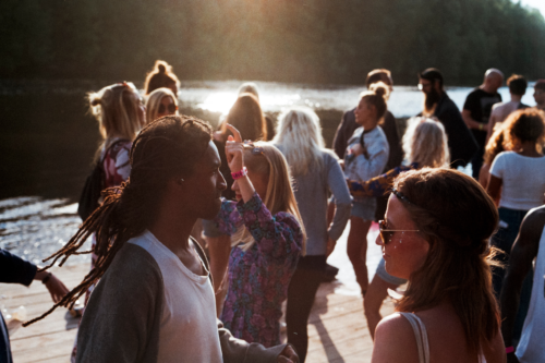 Outdoor party scene at dusk, with a lot of people in T-shirts and sunglasses near a lake.