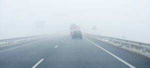 Foggy gray road, cars driving vanish into the fog