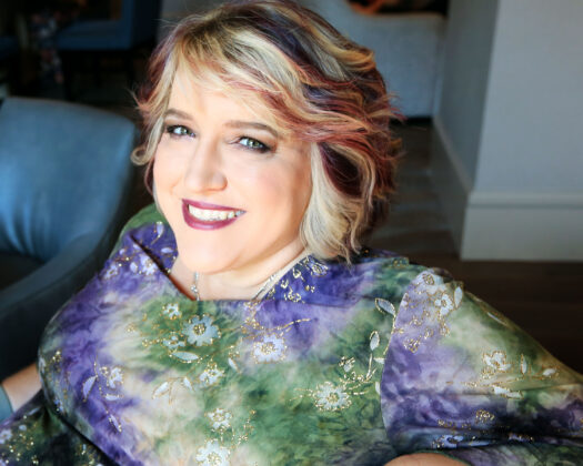 seated, smiling woman wearing purple and green shirt