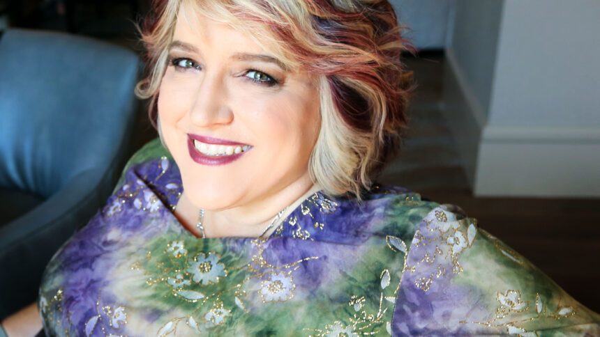 seated, smiling woman wearing purple and green shirt