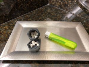 A silver tray holding a green travel oothbrush and gray container full of chewable, white toothpaste tablets.