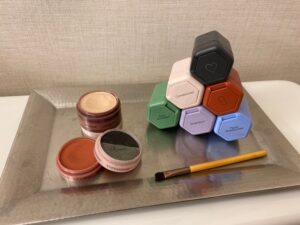A rectangular metal tray holding six interlocking hexagonal cells to fill with carry-on liquids, and a compact stack of discs that fit together, each disc holding a different type of makeup.