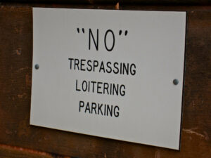 A black and white sign that says "NO" Trespassing, Loitering, Parking.