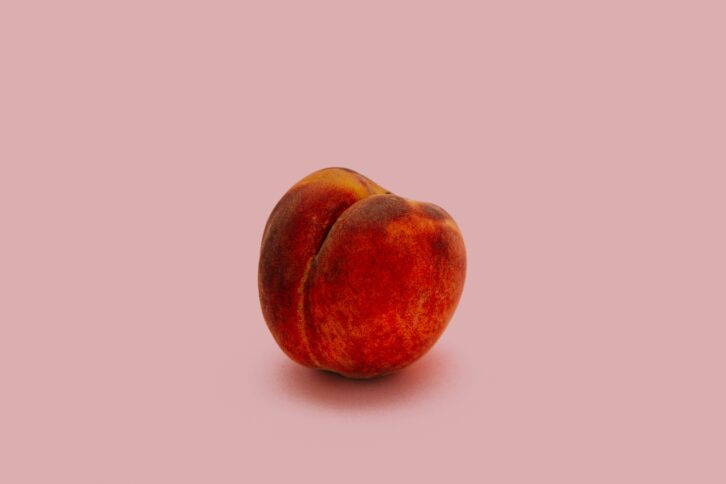 An image of a perfect, whole peach against a pink backdrop.