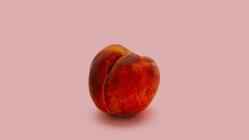 An image of a perfect, whole peach against a pink backdrop.