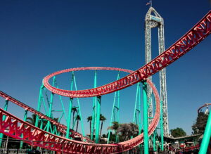 A turquoise and red loop-de-loop rollercoaster with a sunny blue sky in the background.