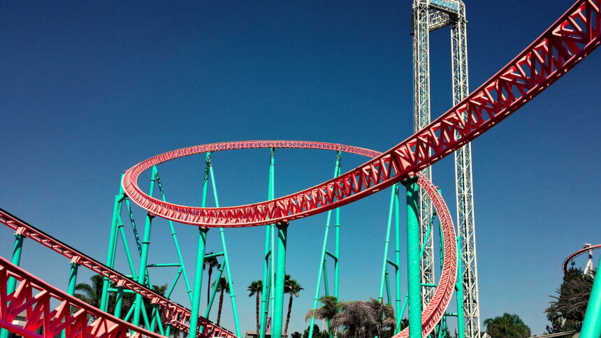 A turquoise and red loop-de-loop rollercoaster with a sunny blue sky in the background.